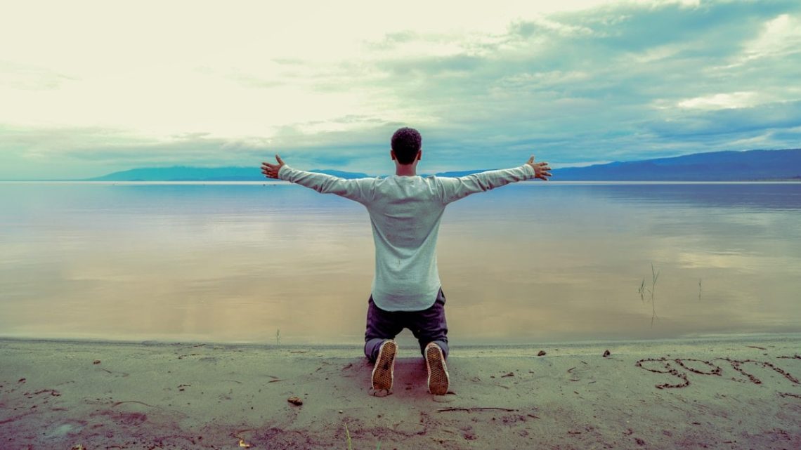 man wearing gray long-sleeved shirt beside seashore during daytime