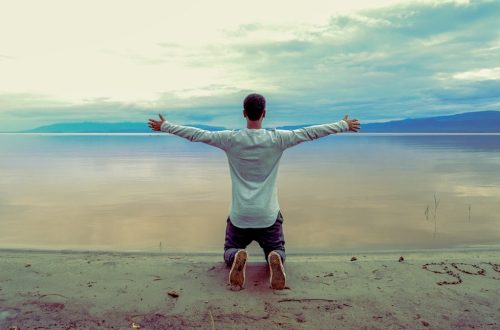 man wearing gray long-sleeved shirt beside seashore during daytime